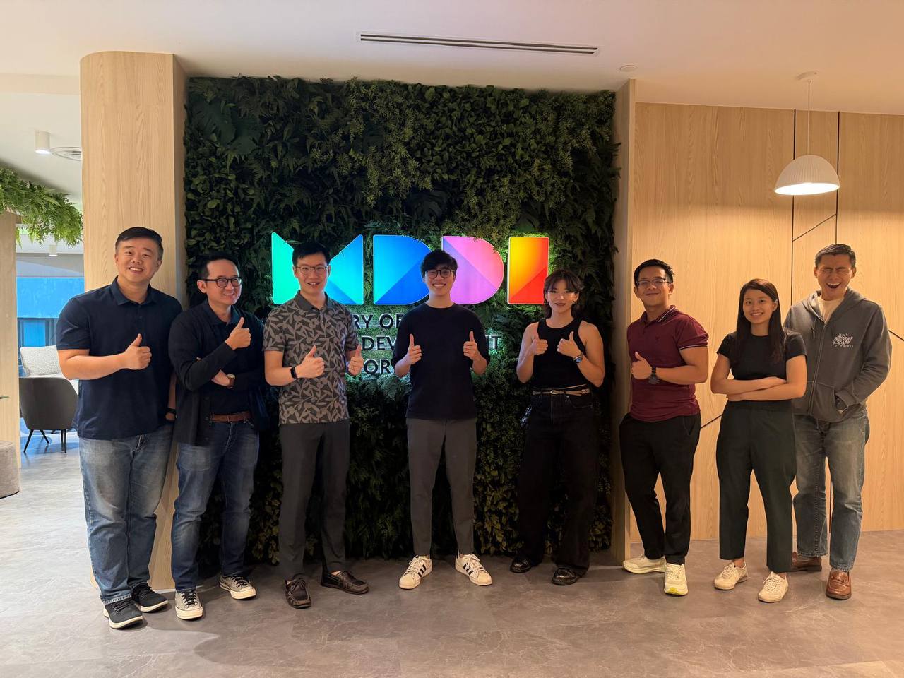 Jordan and colleagues from MDDI's Smart City Division posing together in front of the MDDI logo wall in their office lobby